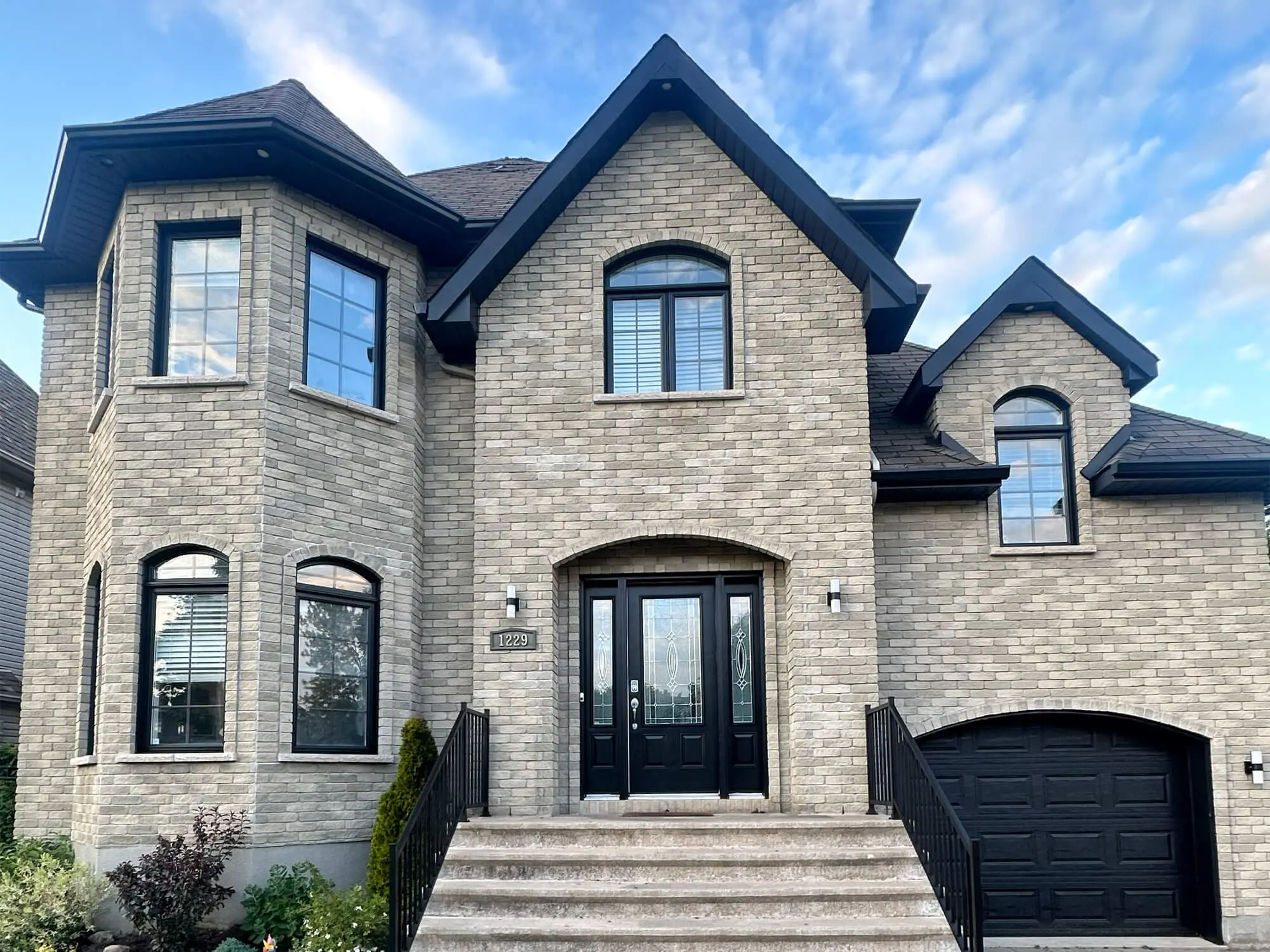 Luxury stone estate exterior featuring black window trim, matching garage door, and professional curb appeal painting by Pro Paint Plus.