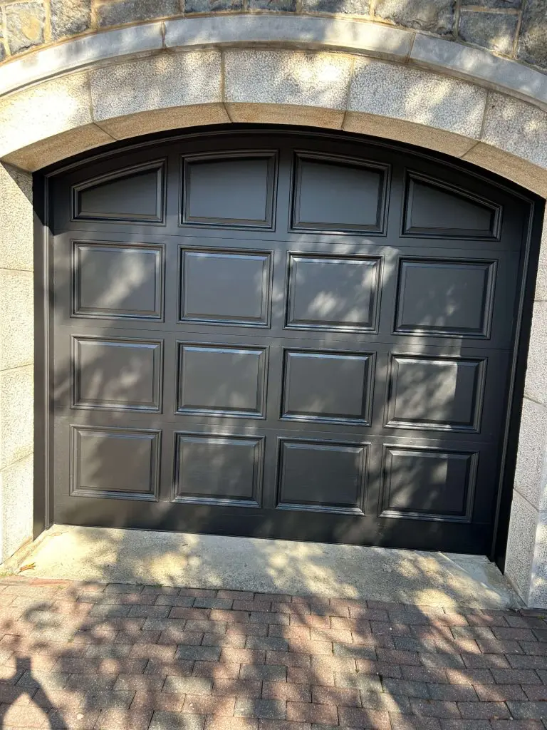 Arched matte black garage door with raised panels expertly refinished by Pro Paint Plus against a stone exterior.