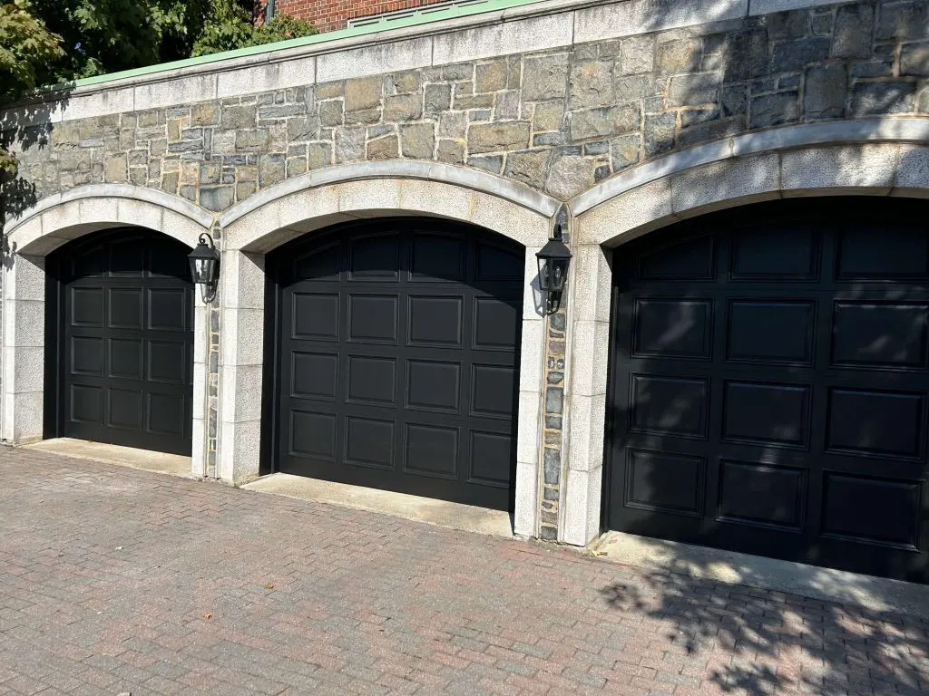 Three elegant black garage doors professionally painted by Pro Paint Plus set within arched stone masonry.