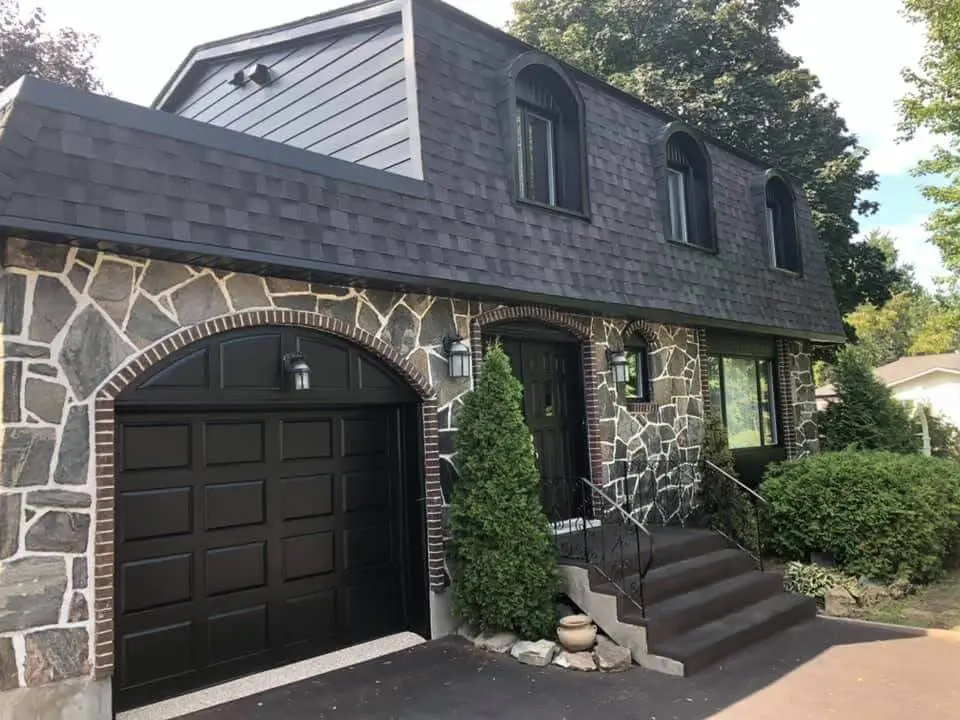 Stone veneer house featuring a black arched garage door and matching exterior trim professionally refinished by Pro Paint Plus.
