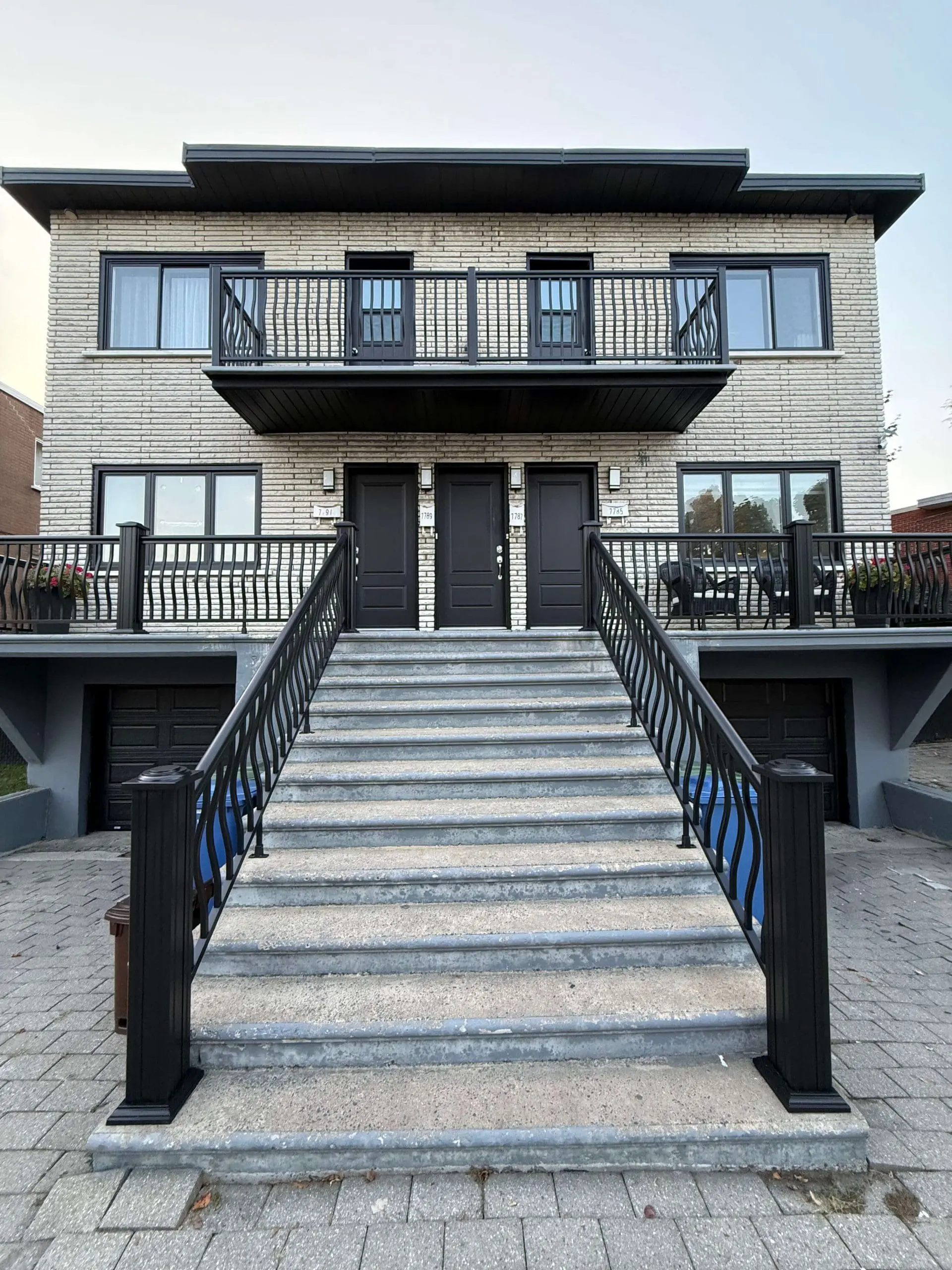 Immeuble résidentiel multi-unités moderne avec peinture extérieure professionnelle par Pro Paint Plus sur les portes noires, les cadres de fenêtres et les balustrades métalliques ornées.