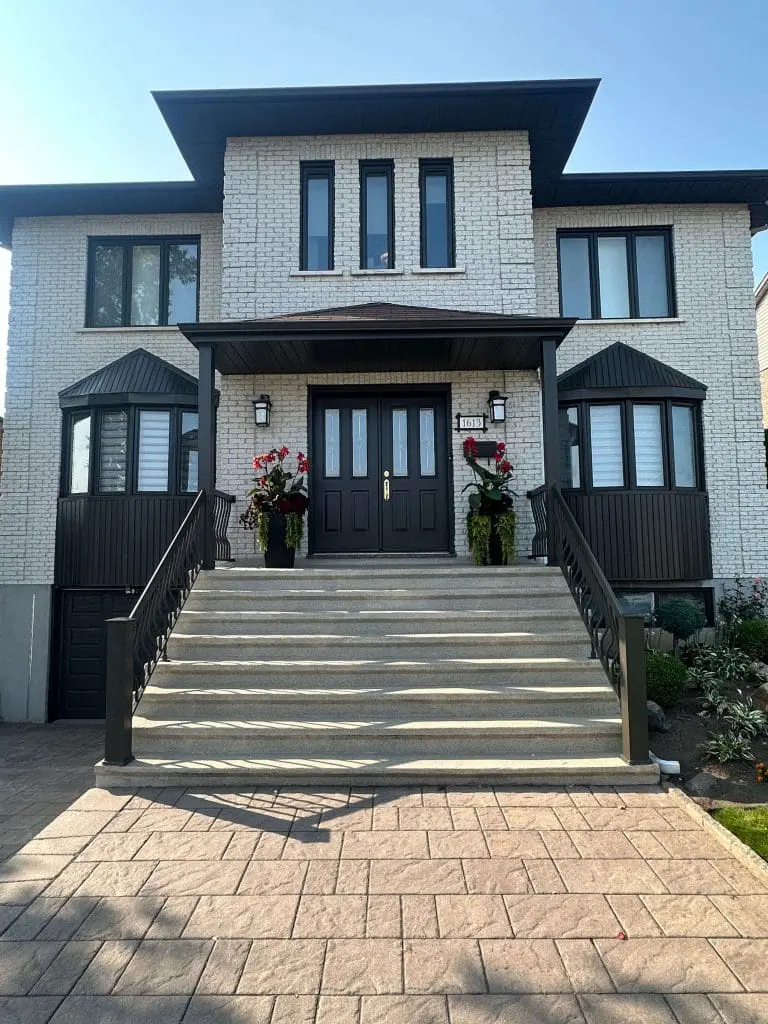 Stately two-story white brick residence featuring a grand stone staircase and bold black architectural accents, meticulously painted by Pro Paint Plus.