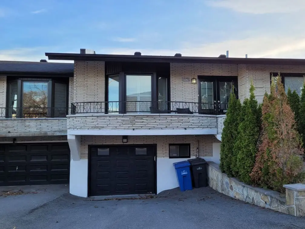 Modern mid-century home exterior featuring a sleek black garage door and balcony trim against light brick, masterfully finished by Pro Paint Plus.