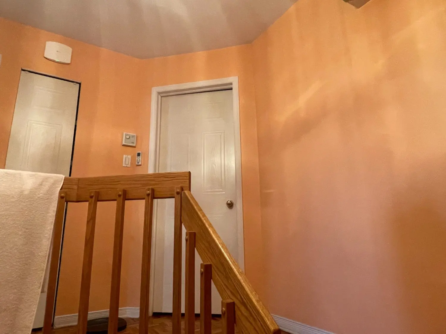 Application professionnelle sur un mur de couloir par Pro Paint Plus, mettant en valeur une peinture au fini satiné pêche éclatant contrastant avec des boiseries blanches et des rampes en bois.