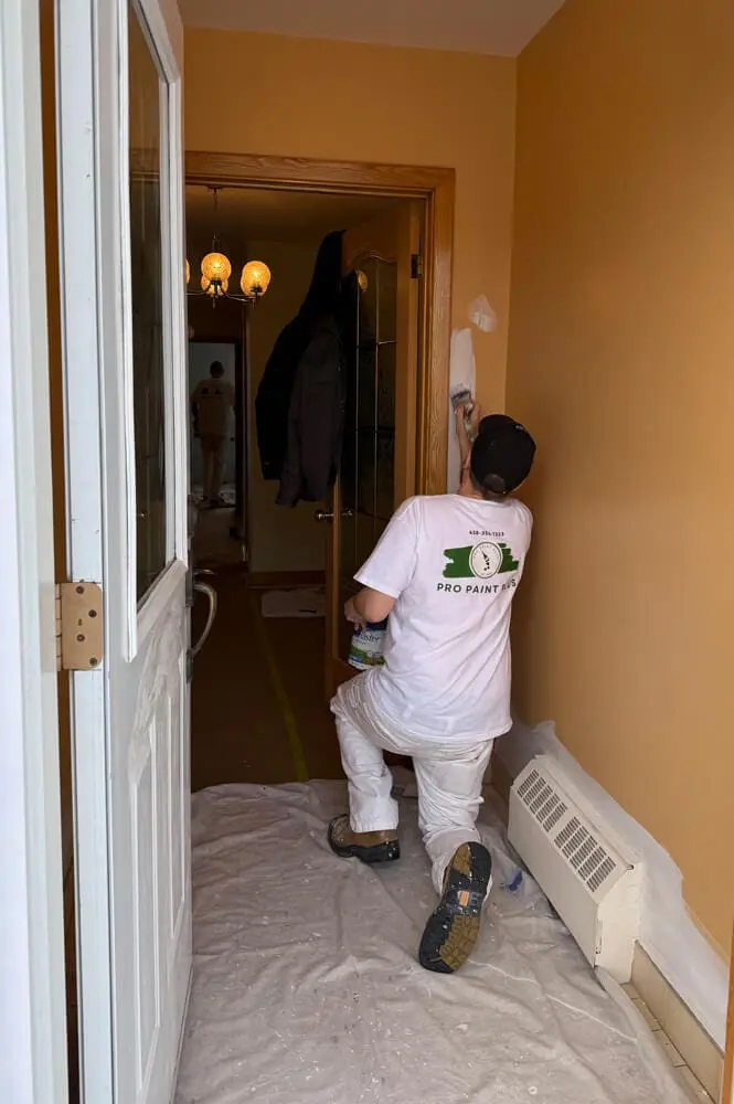 Professional interior painter from Pro Paint Plus carefully cutting in white paint along a hallway door frame.